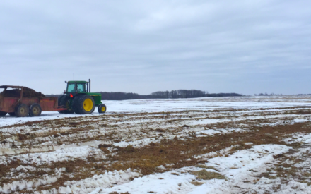A tractor pulls a wagon spreading manure across a snow covered field