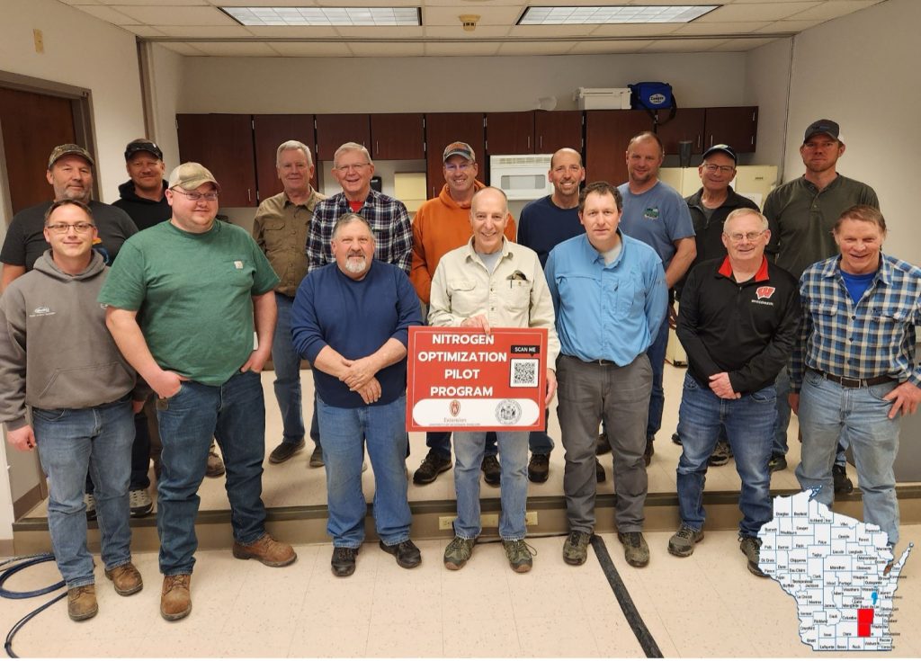 Group of agricultural professionals posing with nitrogen optimization program sign indoors