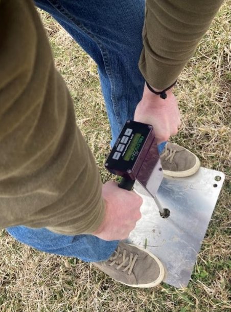 Top-down view of a person pressing an instrument to measure hardness into a pasture with both hands