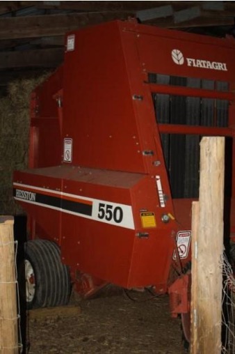 Red Hesston round baler (model 550) stored inside a barn