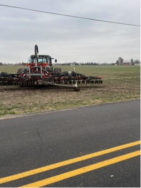Red tractor with manure spreading equipment working in field beside road