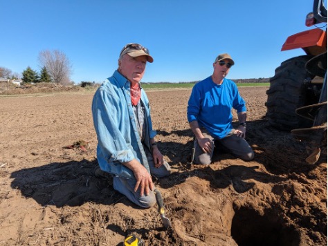 Two men kneeling in plowed field examining soil conditions