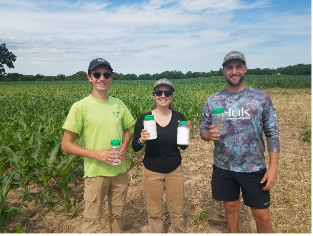 Three researchers holding sampling containers in a corn field