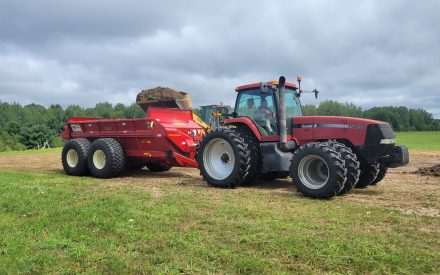 A red tractor applies sludge to a farm field.