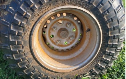 Close-up of a rugged tire with deep treads and orange dust in the wheel well.