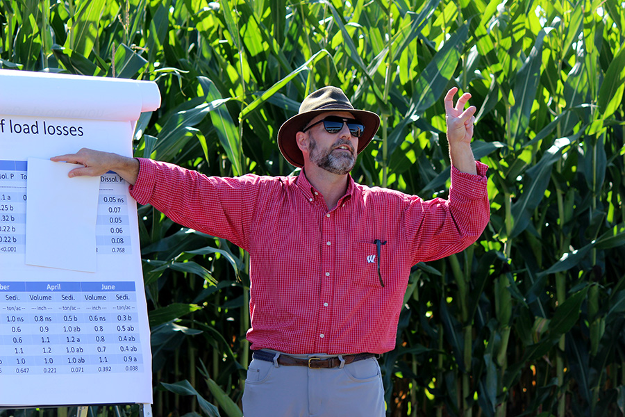Man in red checkered shirt pointing to flip chart with table showing solids, volume, and sediment load data.
