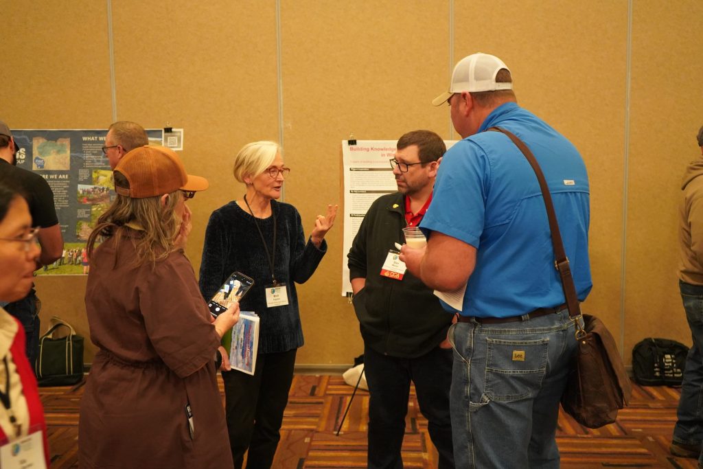 Four people have a discussion in front of an academic poster at a conference.