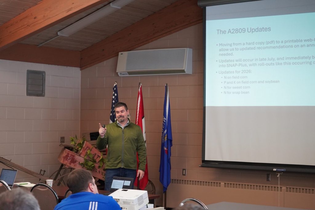 Matt Ruark, PhD, gestures while presenting "The A2809 Updates" slide covering 2026 fertilizer recommendation changes at a processing crops meeting.