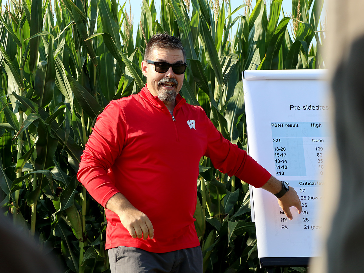 Presenter in a corn field points to a chart showing pre-sidedress nitrogen test (PSNT) results and critical levels.