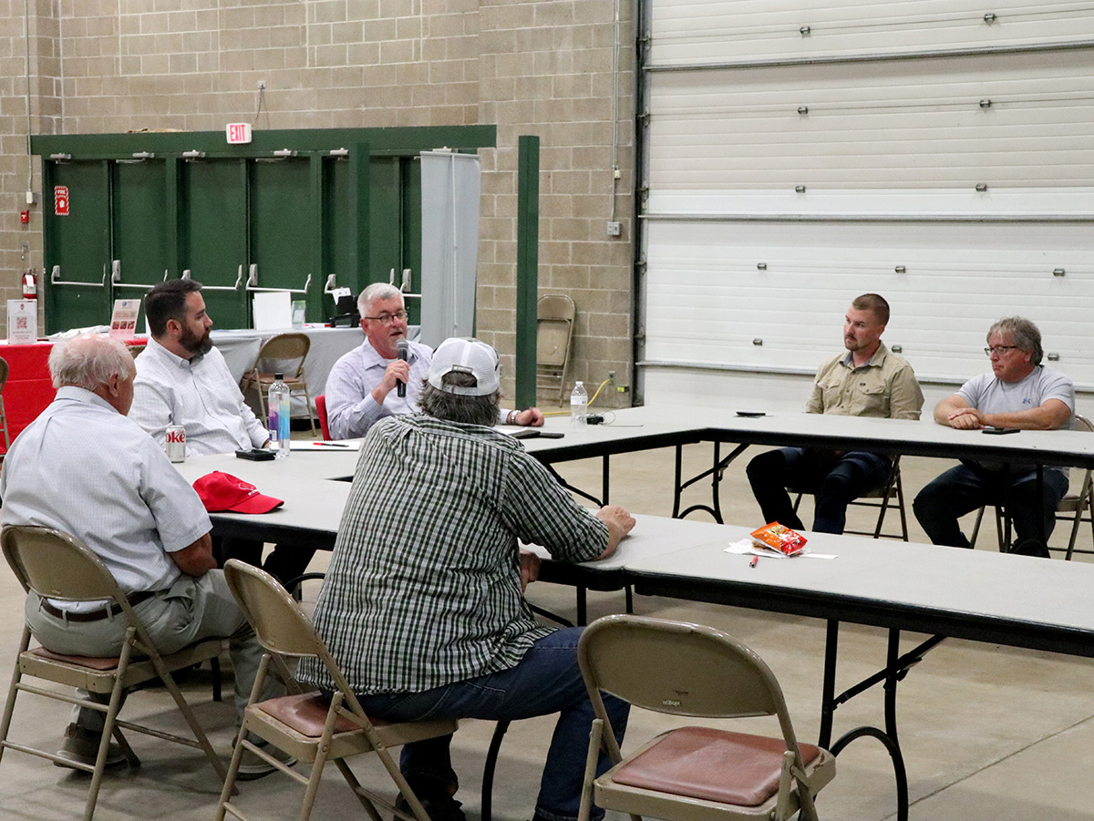 Field day attendees participate in a panel discussion seated around tables inside an agricultural facility.