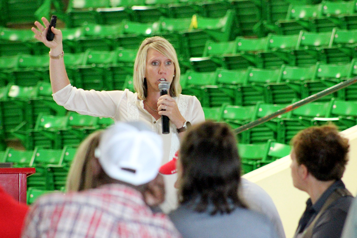 Presenter speaks into a microphone and gestures during an agricultural workshop at an indoor venue.