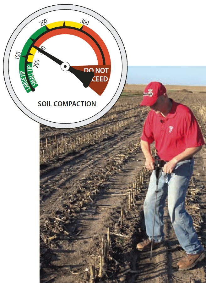 Person using a cone penetrometer in a harvested cornfield to measure soil compaction; inset gauge shows safe, caution, and ‘do not exceed’ zones.